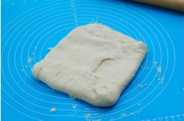 5、可颂,将面片两端向内折，包紧黄油片，捏紧接缝处。