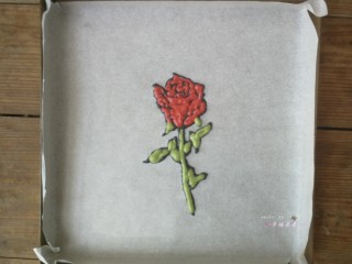 14、彩绘玫瑰蛋糕卷,在绘有玫瑰花的油纸反面根据线条勾勒出玫瑰花的形状，先用黑色面糊描边，再用红色面糊和绿色面糊分别填充花瓣部分和茎叶部分，画好后立即送入预热好的烤箱烘烤1分钟定型