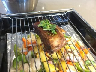 11、法式迷迭香烤小羔羊排,烤箱180预热10分钟。把混合的蔬菜和蒜头倒入铺好锡纸的烤盘里,羊排撒上香菜碎后放在开架上