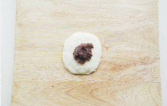 3、【杏仁豆沙面包】,取一个面团摁扁，中间放入红豆沙；