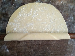 8、手擀面,再擀大一些时，在面饼表面再撒些薄面，用擀面杖卷起并擀平。