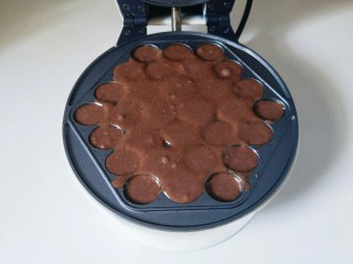 8、#做妈妈的拿手菜#可可颗粒蛋仔,再将做好的可可面糊倒入烤盘模具中，不要太满，否则会溢出。盖上华夫饼盖子，你会发现热水从机器的边缘往出冒，待热水消失，即可将机器断电。