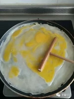 3、无油早餐鸡蛋煎饼灌饼,开中火,等面糊结成片状微微泛白后,敲一个鸡蛋,也用耙子慢慢摊均匀。