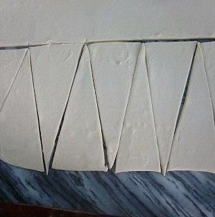 9、可颂,将3次3折后的面团擀成大的长方形的薄面片,用刀切成三角。