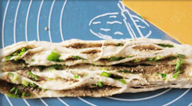 8、手撕芝麻葱油饼,将饼皮从一边卷起成长条型，从中间剖开，切面朝上并在一起