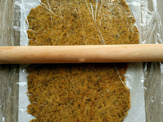 6、海苔全麦苏打饼,桌面铺上油纸，再放上发酵好的面团按扁，最后盖上保鲜膜，将面团擀成2mm左右厚的薄片。