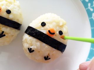 7、肉松小鸡饭团—带给宝宝更多有趣的童年回忆,开始剪鸡爪，直接把海苔折叠，剪6个小细条，最后3个、3个组装在一起就好啦。组装表情的时候，用镊子最方便，没有就直接用手吧。然后把胡萝卜薄片焯水烫熟，用吸管（一般酸奶吸管都会比较硬）摁出嘴巴，中间可以贴上用海苔剪的细条。最后用番茄酱稍稍点一下脸颊，感觉就出来啦（此步可省略哈）
