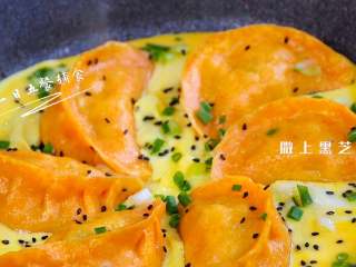 2、抱蛋煎饺,让蛋液铺满整个锅底，蛋液凝固后，撒上葱花和黑芝麻。这个过程1分钟吧。