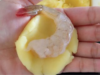 4、凤尾虾球一一烤箱版,取少量土豆泥放在掌心,压平,放入一只腌制好的虾,留尾部,包起搓成圆球