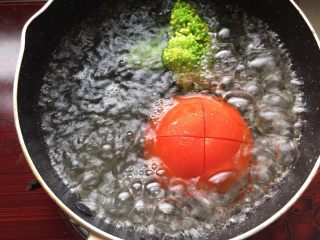 2、三文鱼时蔬蛋黄饼,奶锅烧水,西红柿划十字刀,待水开后放入西红柿和西兰花焯水,完成后捞出备用。
