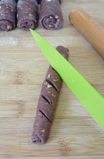 9、【可可果仁面包卷】,竖着卷起成长形面包坯，然后用利刀划几道开口。