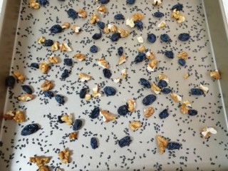14、果干沙琪玛,在烤盘里撒上一部分核桃仁、黑芝麻和葡萄干。