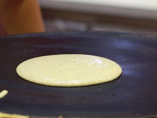 6、美味早餐 妈妈味道的绿豆煎饼果子,饼铛烧热后改小火，在饼铛上滴两滴的油，并用厨房用纸将油抹均匀。用汤勺舀起一勺面糊倒在饼铛上。