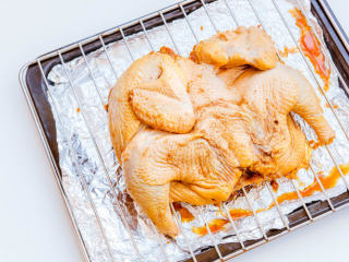 7、烤鸡,取出腌制好的鸡，放在烤架上，底下放烤盘并在下方铺一层锡纸（滴落的油脂不会直接弄脏烤盘，方便后续的清理工作）