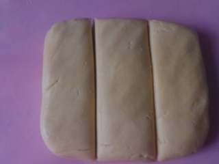 4、彩虹爱心饼干,把面团从盆中取出，放到垫板上，用手揉捏成团，然后分成三份。