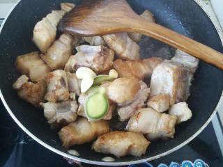 8、#那一抹家乡味#妈妈菜干豆角烧肉,继续加入一些蒜瓣和和生姜，中火翻炒。