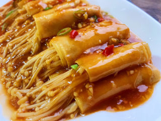 15、豆皮金针菇卷,把锅中的汤汁均匀淋到豆皮卷上面，最后撒点葱花和小米椒点缀。