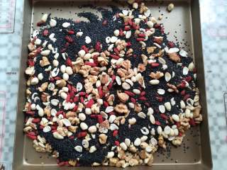 5、核桃花生芝麻糖,把黑芝麻倒进装有核桃，花生和枸杞的金盘里，放入烤箱调到发酵档位保温