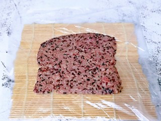 12、血糯米粢饭团,将席卷上铺上一张保鲜膜,放上血糯米,压平整。