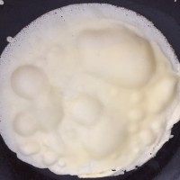 6、芒果千层蛋糕,把面糊倒入。最好用一个勺子。每一张都放一勺面糊。这样煎好的冰皮大小一致。只需一面煎即可。然后依次煎好所有的面皮。