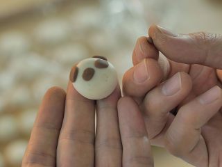 5、 熊猫汤圆,这时候再把巧克力色的面团拿出来，做出熊猫脑袋和熊掌。圆的小白面团就做熊猫脑袋，压扁了的就做熊掌，熟练后一会儿功夫就都搞定了～