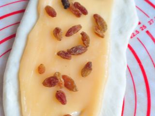 10、葡萄干麻糬软欧,将麻糬馅也分成三份，擀开后放在面皮上，最上面撒些葡萄干。