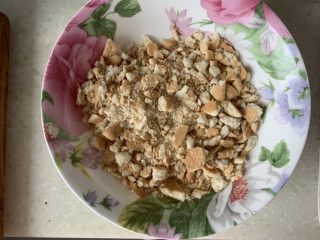3、芒果慕斯蛋糕,饼干捏碎，或者使用擀面杖，变成饼干末，最好用奥利奥饼干（去掉夹心）、消化饼干等，因为没法出门采购，用了姥姥的青食钙 奶 饼干，这种饼干用擀面杖不好使，纯手工捏碎，建议捏的再碎一点，吃起来口感会更细腻，加入融化的黄油，搅拌均匀。准备6寸活底模具，模具底下垫一张等大的油纸，将拌均匀的饼干放入，压实，放入冰箱冷藏备用。