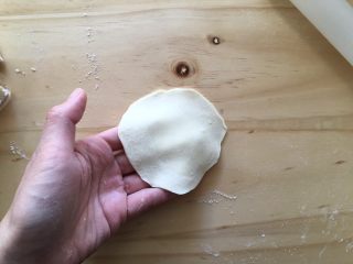 11、手工牛肉水饺,左手拿着面皮，右手用擀面杖擀，擀成中间稍微厚一点，边沿薄的饺子皮