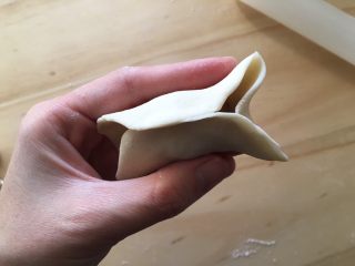 14、手工牛肉水饺,然后如图所示，两边从中间推进去，捏紧，然后凸出来那一小块再从凸出处往里按压捏紧