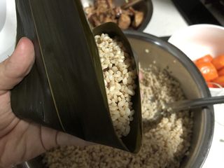 25、蛋黄肉粽,然后一手握住装满料的一端，将多余的叶子向前折