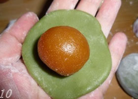 10、冰皮月饼,手上取一些手粉，将一块面团按扁，加入馅料