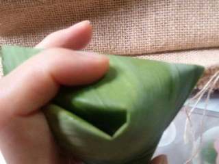 11、蜜枣什锦粽子,把多余的粽叶顺着折叠，包裹成三角形。