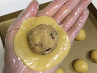 16、蔓越莓椰蓉月饼,取一份饼皮面团，放在掌心，用另一只手轻按压面团，拍成圆饼状，放上一份蔓越莓椰蓉馅。