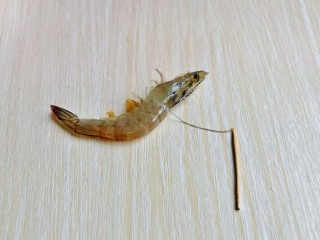 2、爆炒基围虾,首先我们去虾线,可以借助一根牙签,从头部与身体间的位置将虾线挑出,如图所示。
