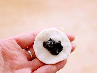 10、萌猪黑芝麻汤圆,取一块醒发好的白色面团、按成饼状后包入黑芝麻馅料