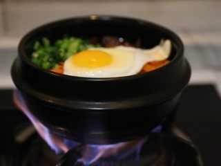 15、腊肠石锅拌饭,放上炒好的香菇／腊肠／青菜／胡萝卜和准备好的韩式辣萝卜，放在炉子上小火加热至米饭四周出现焦黄香气即可。