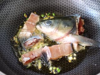 6、炖草鱼,锅烧热后倒入花生油烧热,先爆香葱姜丝,再倒入鱼头和鱼排,小火煎至两面变白。