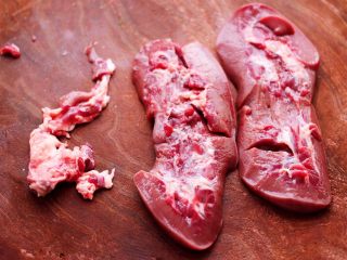 3、孜然香辣烤猪腰串,把冲洗干净的猪腰,用刀切成两半,把猪腰的筋膜切掉不要。