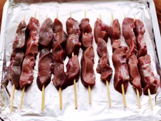 11、孜然香辣烤猪腰串,依次串好所有的猪腰串,烤盘上铺上一层锡纸,把 串好的猪腰串放到烤盘里。