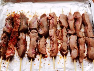 15、孜然香辣烤猪腰串,烤制到10分钟的时候,把猪腰从烤箱取出来,再次把猪腰串翻过来,撒上孜然粉和辣椒粉。