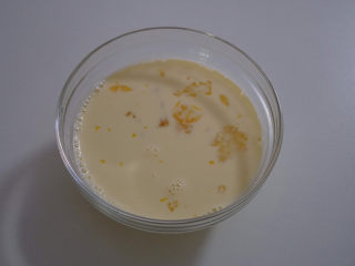 5、一次就成功的芒果牛奶布丁,把热好的牛奶倒入打散的鸡蛋中，继续打散，并挤入少许的炼乳。