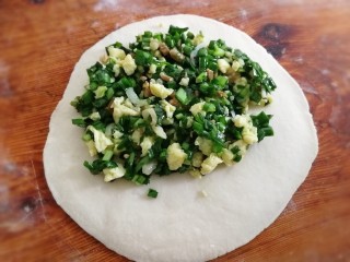 13、韭菜盒子,取一个面剂，滚圆、按扁，擀成中间微厚四周薄的圆形，放入拌好的馅料。