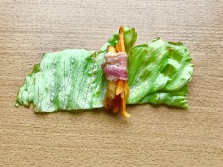 18、薯条的N种吃法,当培根卷起边就可以出锅了。然后如图先横放着生菜，再上面横放培根，放薯条和叮好的胡萝卜丝，卷起培根。