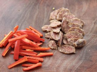 3、香肠辣爆芸豆丝,把红椒去籽后,用刀切丝,香肠用刀斜切成薄片,香肠我是提前蒸熟的,放在冰箱冷冻,随吃随取特别方便。