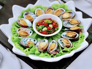 14、白灼鲍鱼,盘子底下铺上生菜，把煮熟的鲍鱼捞出沥干水分，放入鲍鱼壳里摆盘，中间码放调制好的蘸料汁就可以享用咯。