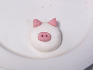 8、元宵节~萌萌哒卡通【小猪汤圆】 ,分出来 1g或者更少,揉成椭圆形,稍微按扁一些,放在大面团中间靠下的位置,再用牙签扎两个小孔,小猪的鼻子就做好了。最后是耳朵,0.5g一个,捏成三角形,如图,放在头部耳朵的部位。糯米团很黏,不刷水也可以粘住的