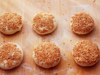 15、果仁红糖发面饼,用手摁扁后,白芝麻放到一个盘子里,把饼蘸上白芝麻。