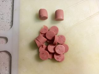1、火腿芝士雪娃娃饭团#诞愿有你#,火腿剥好，头尾的部分切下来，做雪人的帽子，中间部分切片，可以切碎一些更好包。