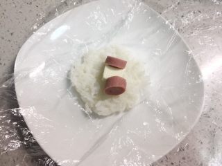 5、火腿芝士雪娃娃饭团#诞愿有你#,再取30克左右的米饭，包入半块芝士小食，两片火腿片，同样的方法团成小一点的饭团。