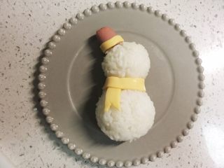 11、火腿芝士雪娃娃饭团#诞愿有你#,再剪一条同宽的小芝士条，围在两个饭团连接处，做围巾的横向部分，围巾就做好了。